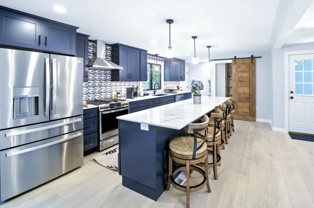 Bright modern kitchen with stainless steel appliances, island, bar stools, and light wood floors.