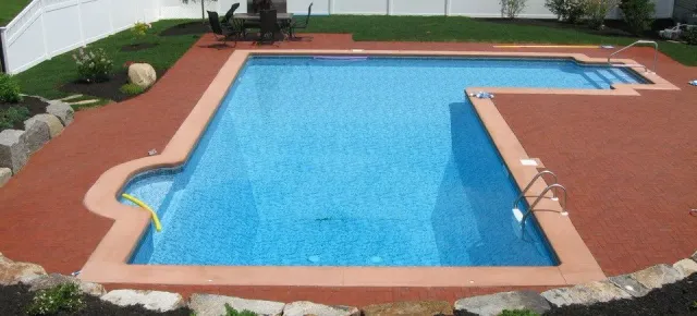 Backyard swimming pool with blue water, red patio decking, and a diving board
