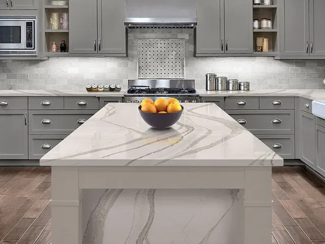 A kitchen with a large island and a bowl of oranges on the counter.