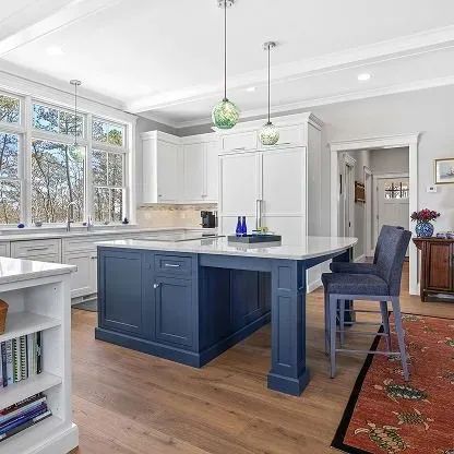 Bright kitchen with navy island, white cabinets, wood floors, and a red patterned rug