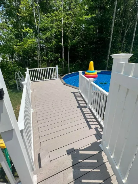 A wooden deck with a white railing leading to a swimming pool