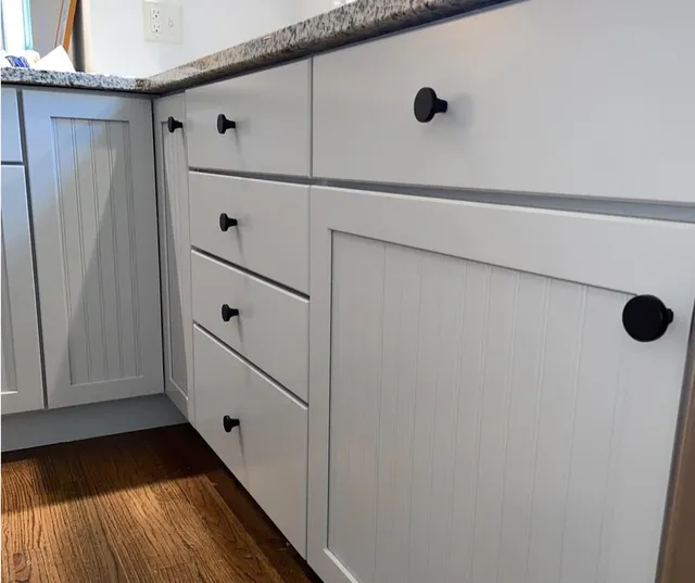 Freshly painted white kitchen cabinets with black knobs and granite countertop in a modern kitchen