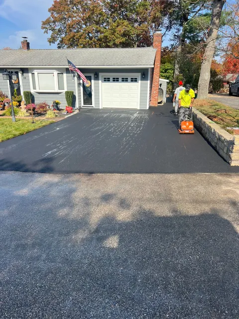 A man is using a lawn mower to cut a driveway in front of a house.