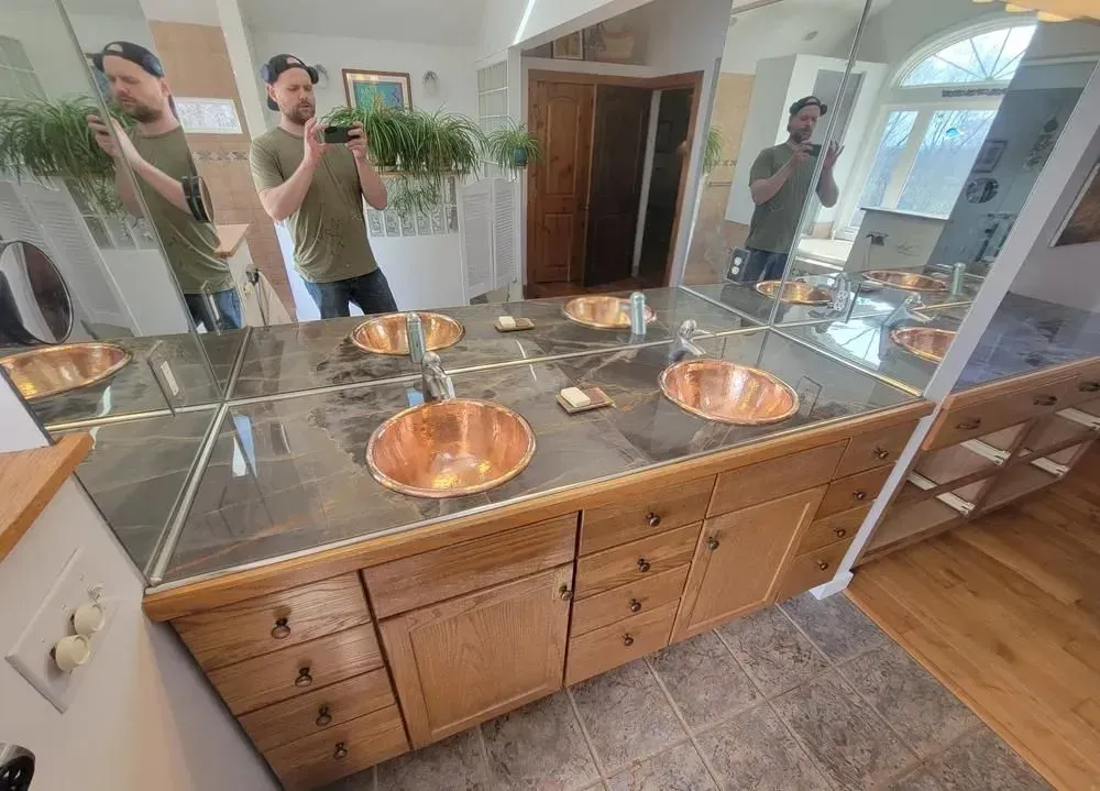 Bathroom vanity with copper sinks, granite countertop, and large mirror reflecting two people taking a selfie