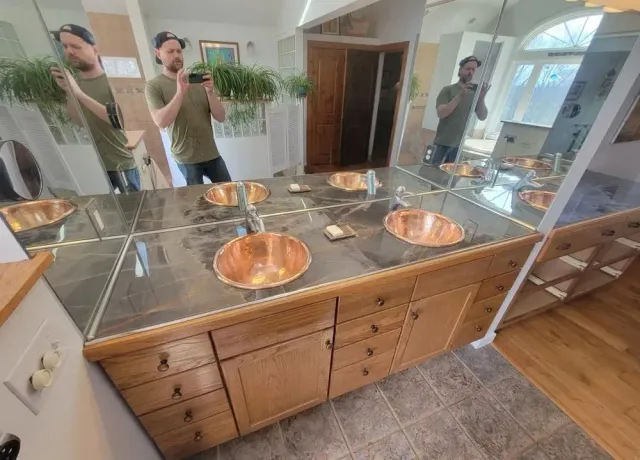 Bathroom vanity with copper sinks, granite countertop, and large mirror reflecting two people taking a selfie