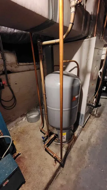 A residential furnace and hot water heater with copper and metal piping in a utility room