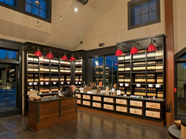 A liquor or wine store with shelves filled with bottles, a wooden checkout counter, large windows, and red lamps hanging from the ceiling.