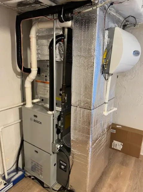 Furnace and attached humidifier in a basement setting, wrapped in reflective insulation.