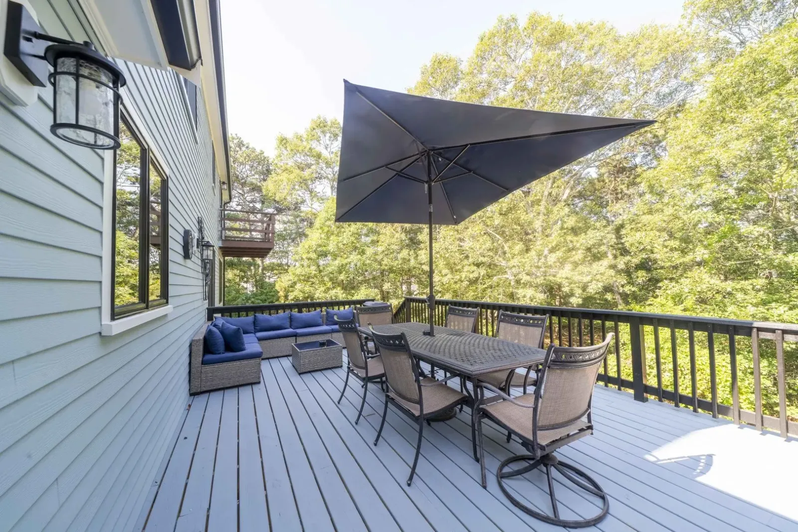 Outdoor wooden deck with patio furniture, blue cushions, and a large black umbrella beside a house.