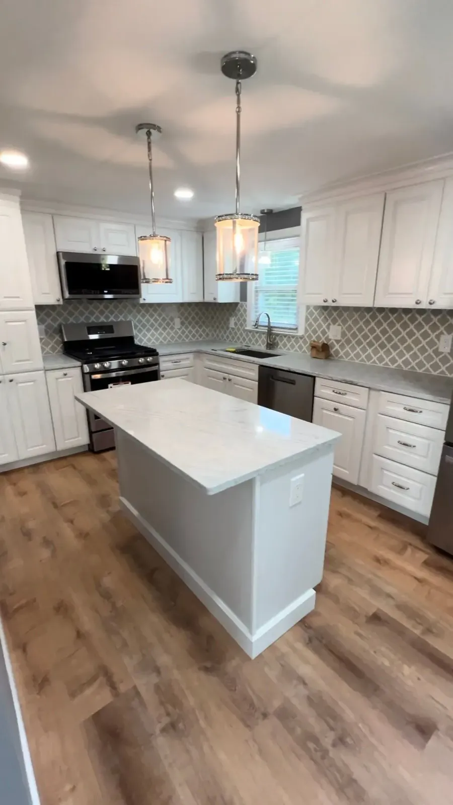 Bright modern kitchen with white cabinets, island, pendant lights, and wood flooring