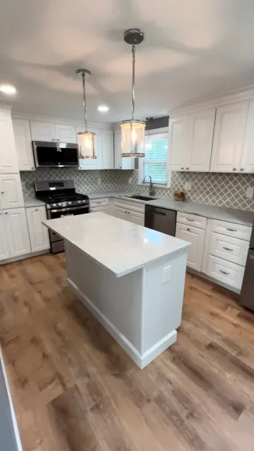Bright modern kitchen with white cabinets, island, pendant lights, and wood flooring