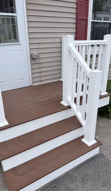 Front porch steps with brown treads, white risers and railing beside a house entrance.