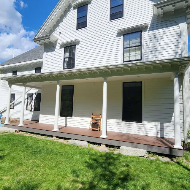 White house with a wraparound porch, white columns, and a wooden chair on the front porch, viewed from the lawn