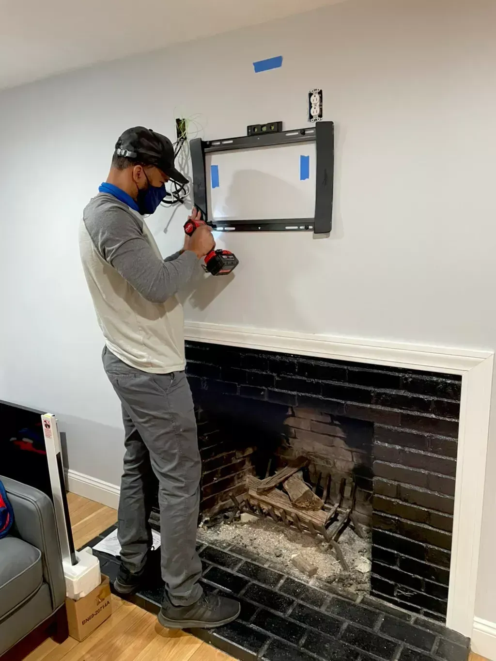 Person using a drill to mount a TV above a fireplace in a living room
