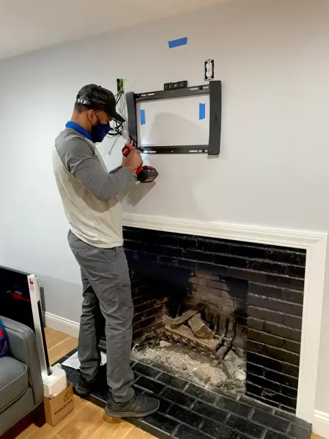 Person using a drill to mount a TV above a fireplace in a living room