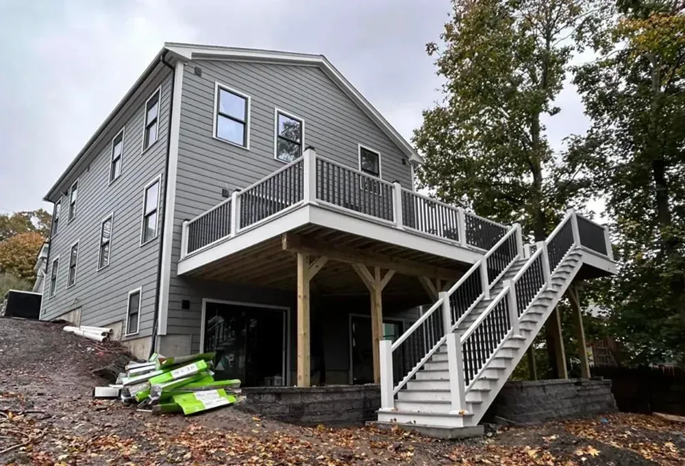 Two-story house with gray siding and large deck with stairs.