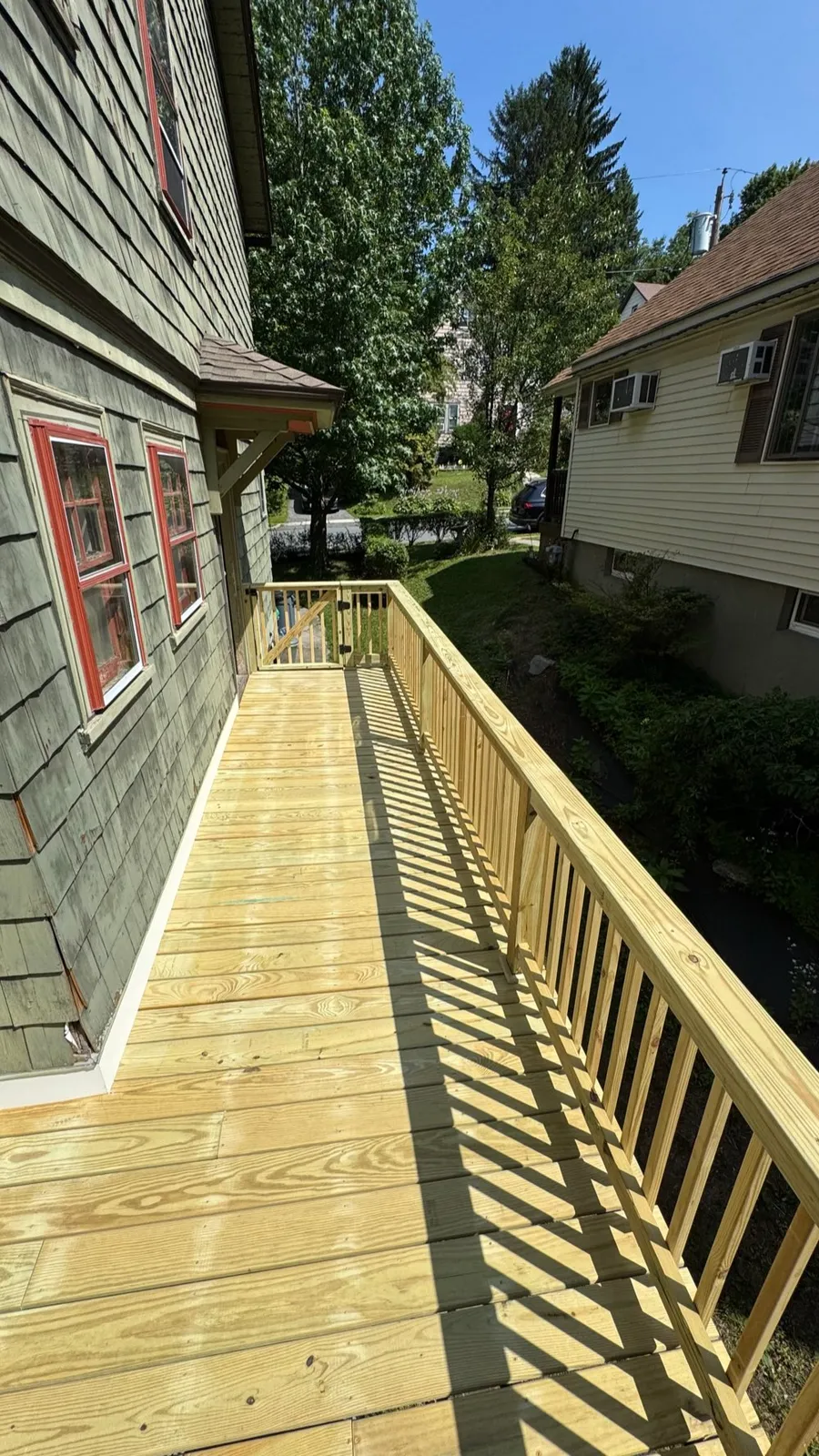 New pressure-treated deck with wood railings beside a shingled house