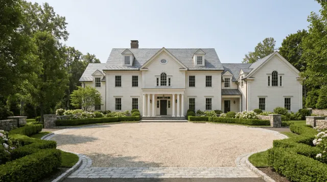 Large white house with a driveway and greenery