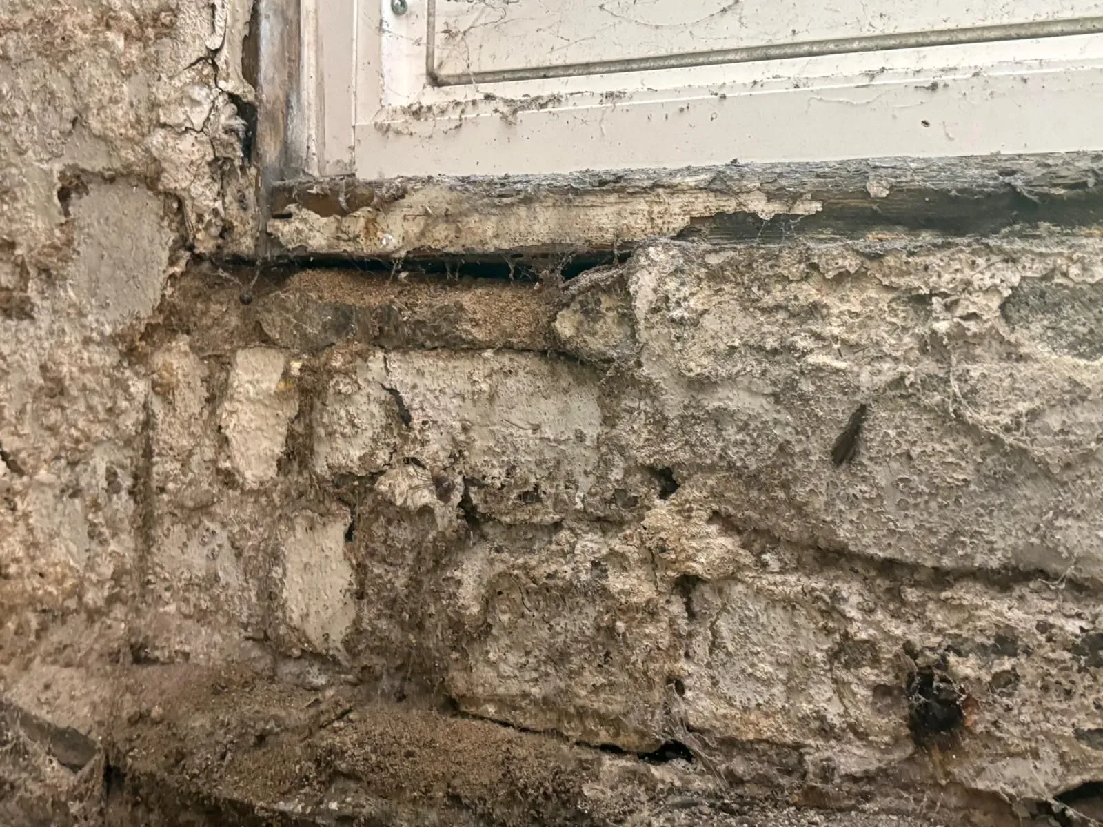 Stone wall with deteriorating mortar and window frame above.