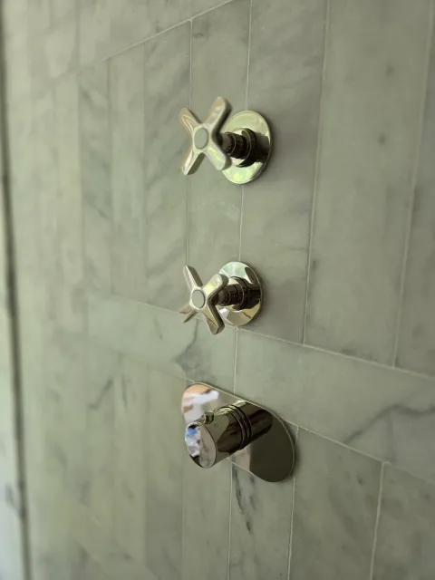 Polished shower controls installed on a marble-tiled wall