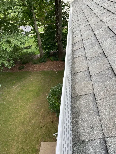 A gutter on the side of a house with trees in the background.