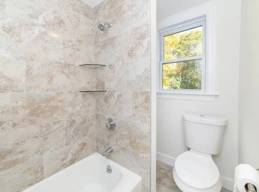 A bathroom with a tub, toilet, shower and window.