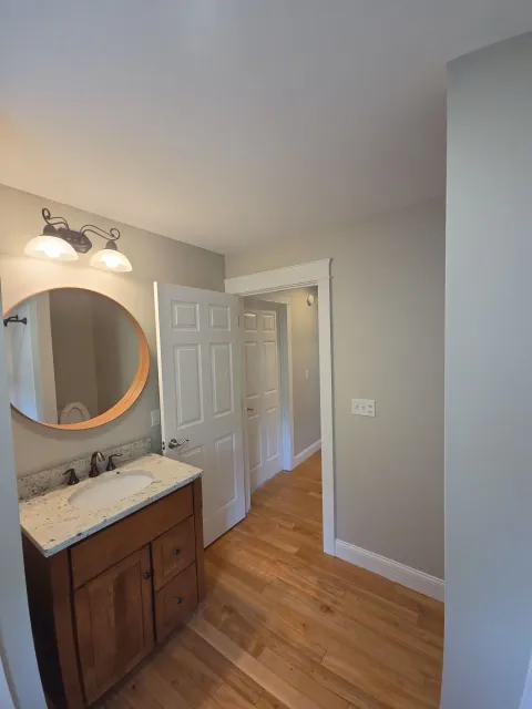 A newly painted residential bathroom featuring a vanity, round mirror, and light gray walls.