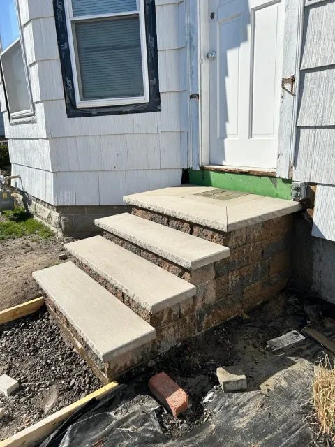 Concrete steps leading to a white mobile home entrance with a brick foundation and green artificial turf