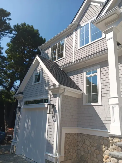 White house exterior with garage, stone foundation, and sunlit windows under a blue sky