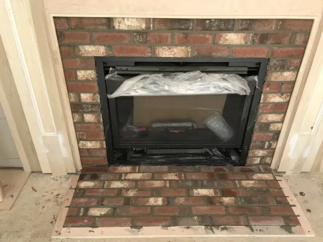 Brick fireplace with black glass insert, surrounded by a brick hearth and white trim.