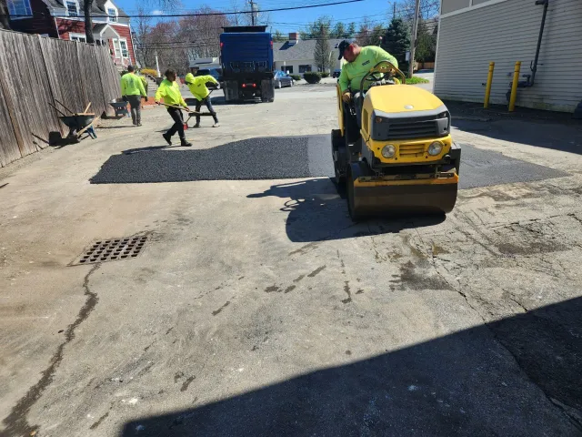 Road crew paving a street, with workers in neon vests and a yellow road roller on fresh asphalt.