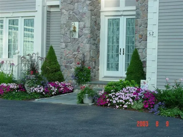 Front entrance with stone facade, glass doors, and flower beds along a driveway