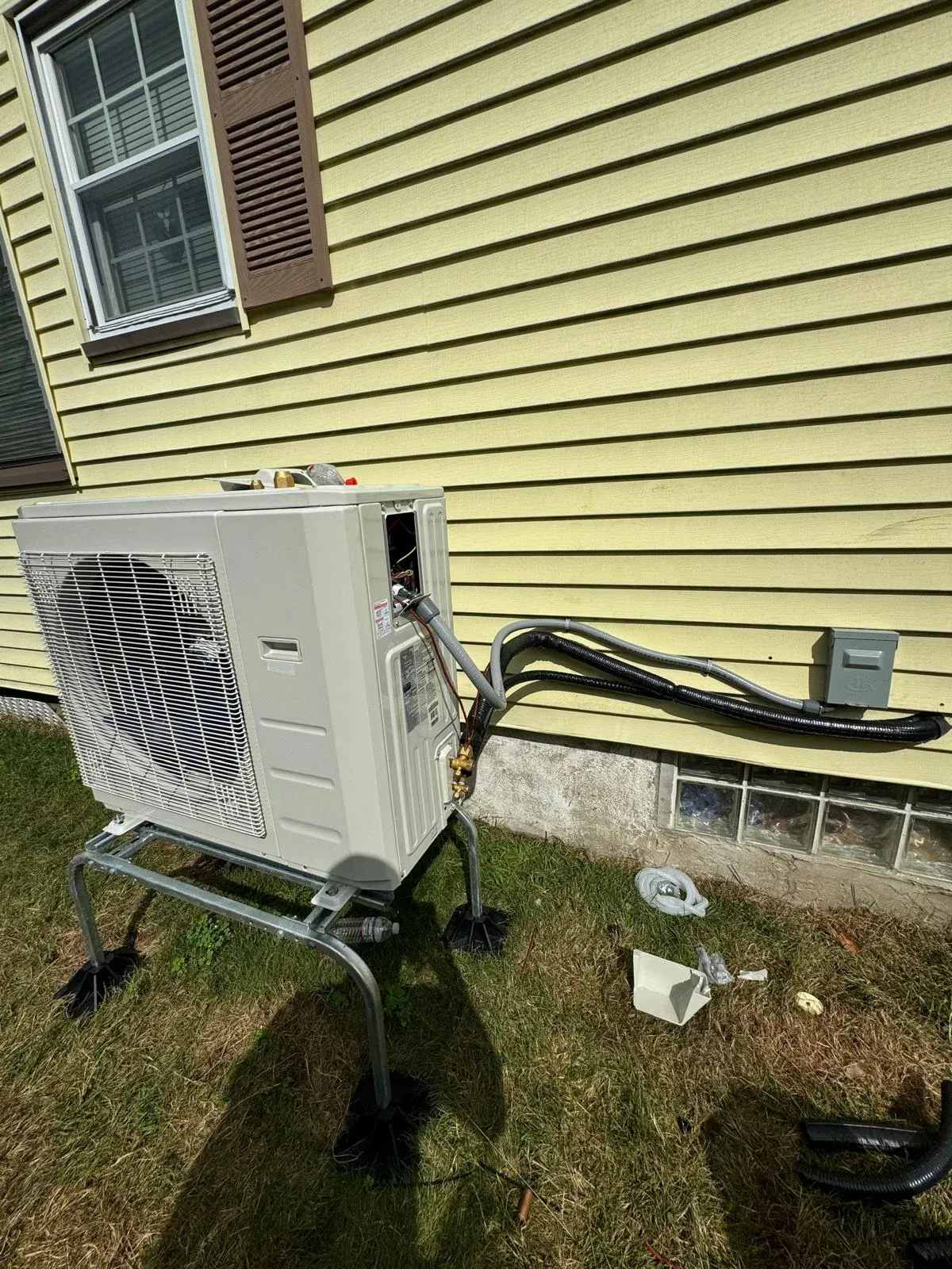 Outdoor heat pump condenser unit installed on an elevated stand beside a house