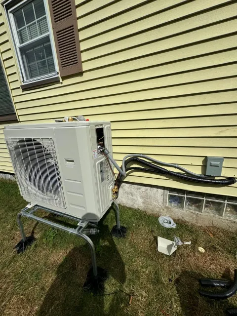 Outdoor heat pump condenser unit installed on an elevated stand beside a house