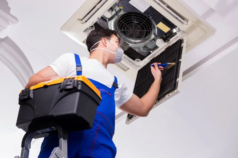 Technician model cleaning an indoor ceiling-mounted HVAC unit