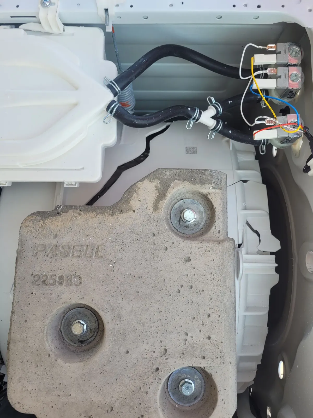 Close-up of a car interior with exposed wiring, a white plastic panel, and a gray metal bracket with bolts.