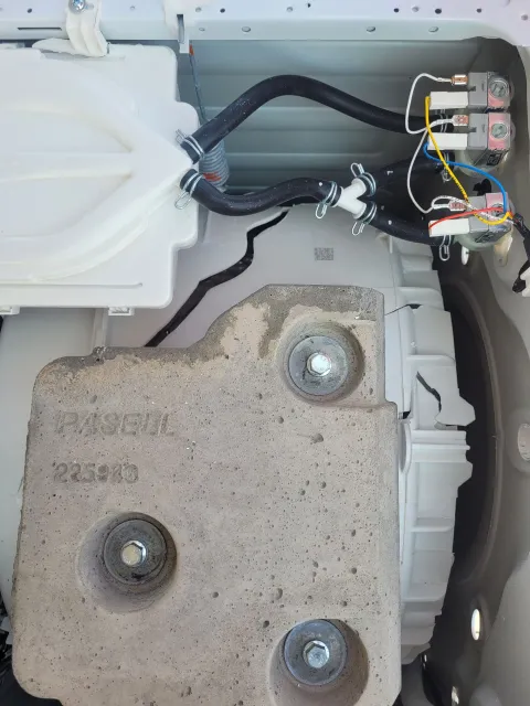 Close-up of a car interior with exposed wiring, a white plastic panel, and a gray metal bracket with bolts.