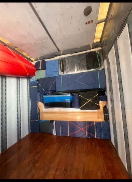Messy storage room with stacked mattresses, blue bin, wooden floor, and metal shelves