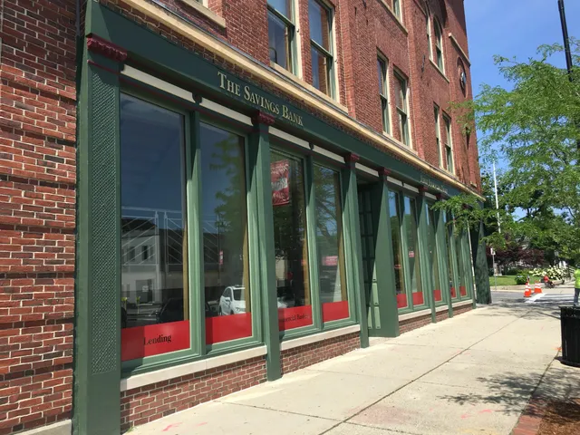 The front of an arch-shaped brick building with red and green windows, featuring a captivating painting.