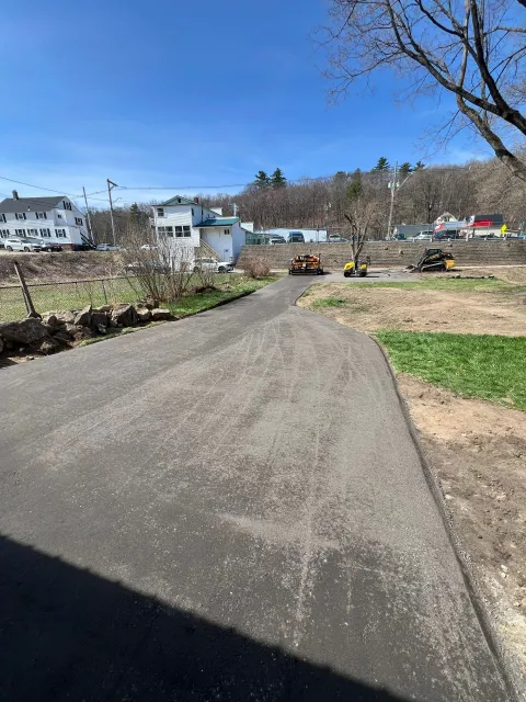 Paved path leads toward buildings and trees under a clear, blue sky.