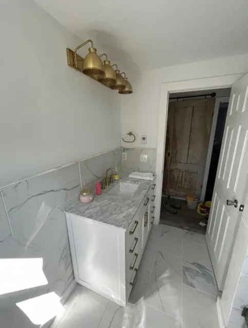 Bathroom with white vanity, marble-look tile, gold fixtures, and a rustic wooden door.
