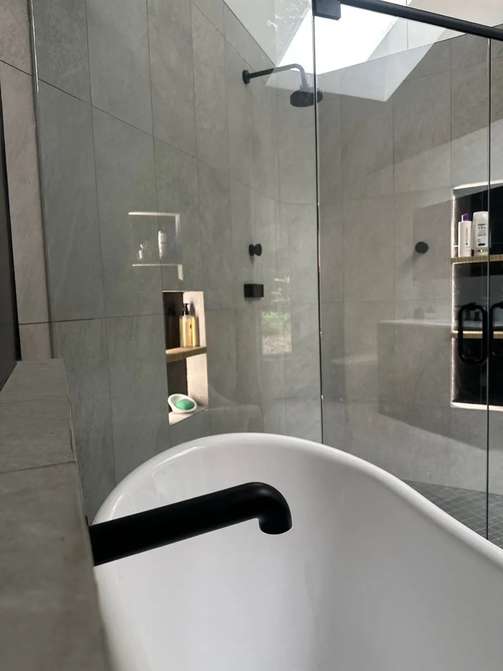 Principal bathroom with large-format grey stone tile, a freestanding soaking tub with a matte black filler, a frameless glass shower and a skylight above