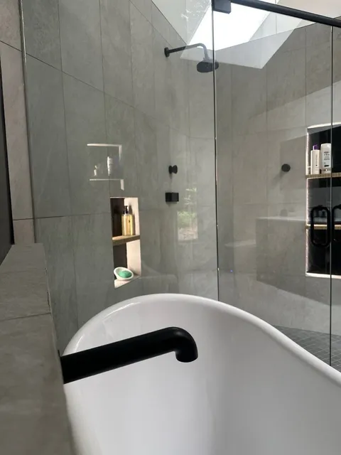 Principal bathroom with large-format grey stone tile, a freestanding soaking tub with a matte black filler, a frameless glass shower and a skylight above