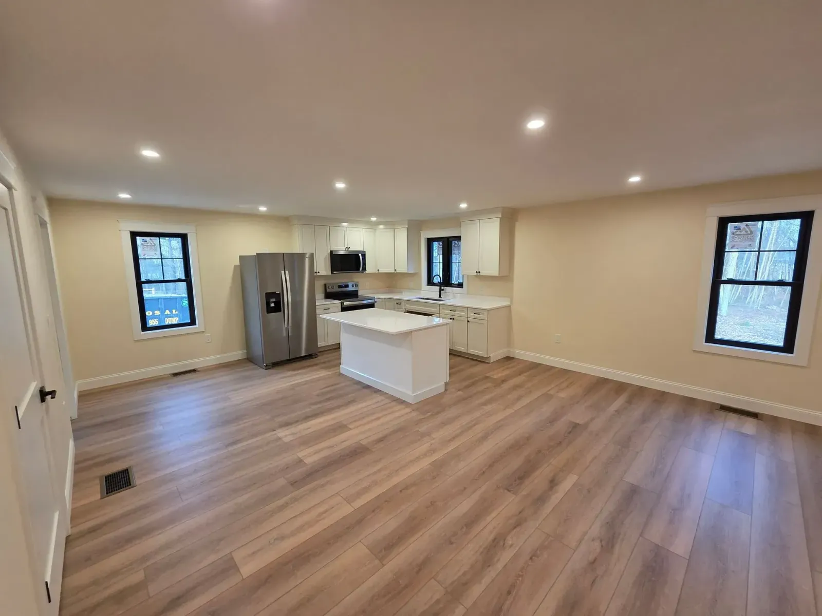 Open-concept kitchen and living area with white cabinets, stainless steel refrigerator, and wood-look flooring.