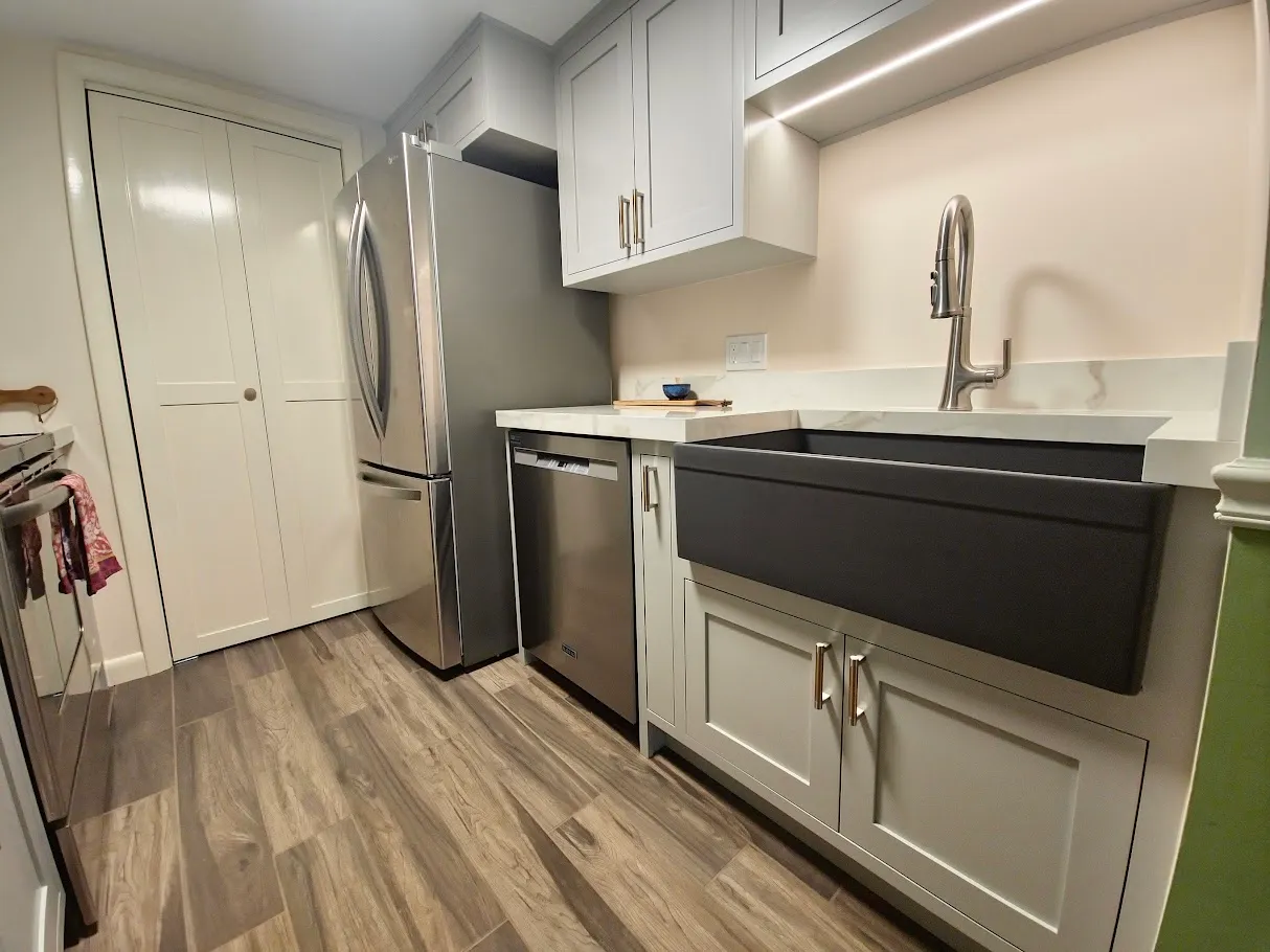 Remodeled galley kitchen with gray shaker cabinets, marble-look quartz counters, and a black apron-front sink in Bristol, Rhode Island by Toensing Construction