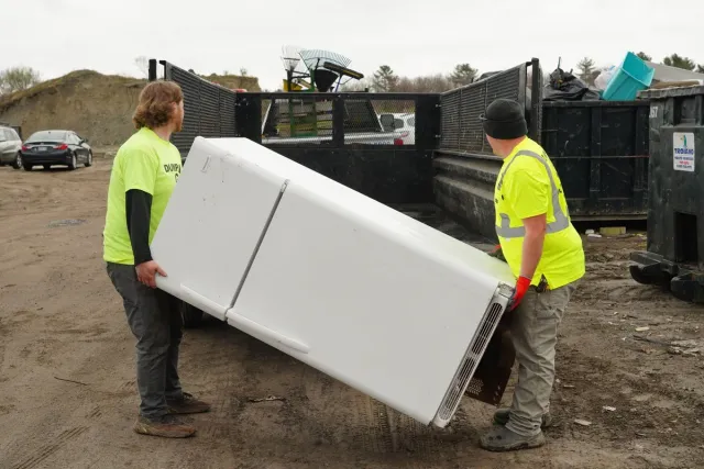 Two Dump Guy employees lifting a while refrigerator