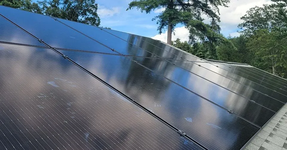 A row of solar panels on a roof with trees in the background.