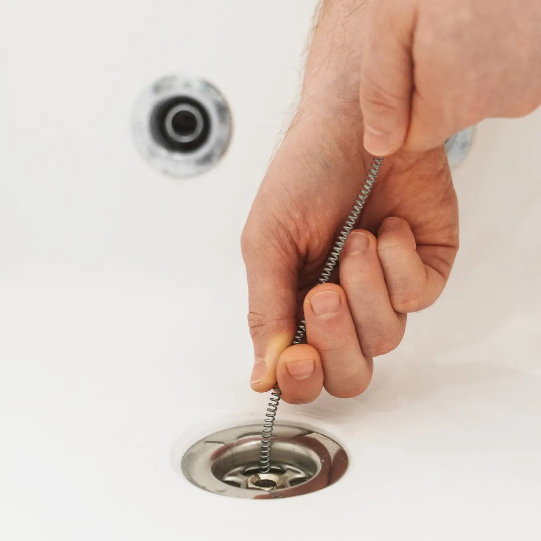 Close-up of a person cleaning a sink drain with a coil brush.