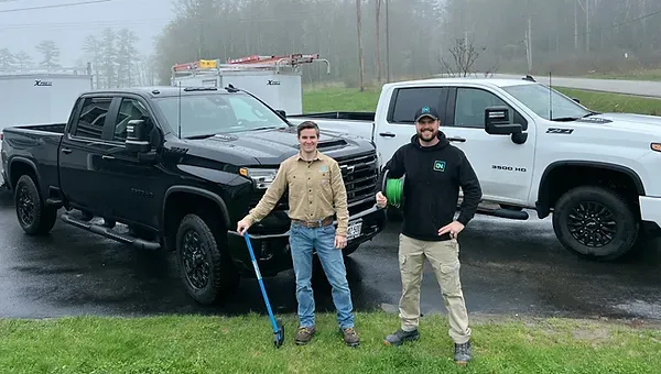 In power employees, Nehemiah and Isaiah smiling in front of In Power electrical service vehicles