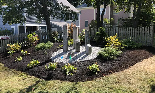 Mulched bed of plants surrounding stones set up as a sculpture in a grassy lawn